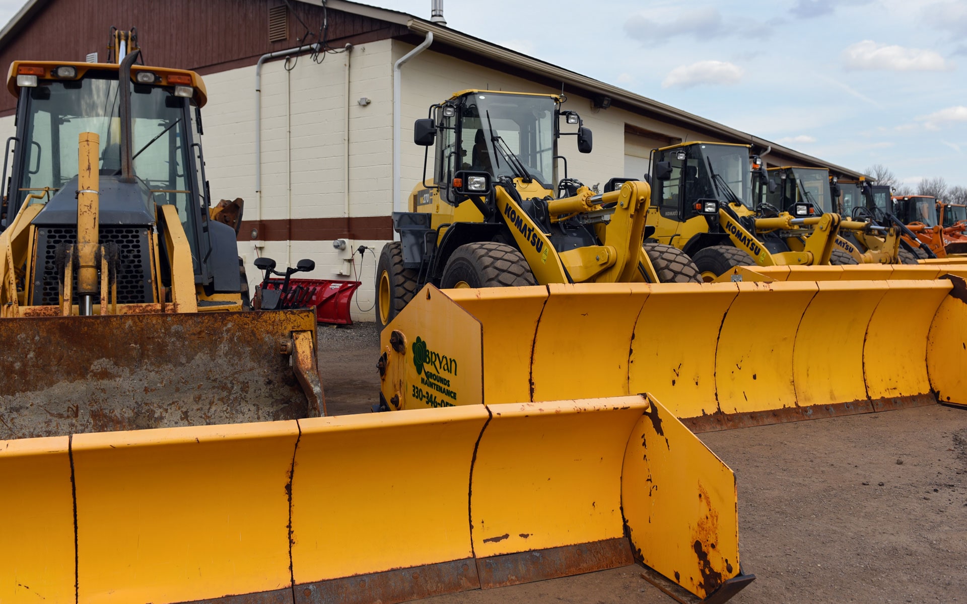 Wheel loaders and pusher blades parked outside the shop